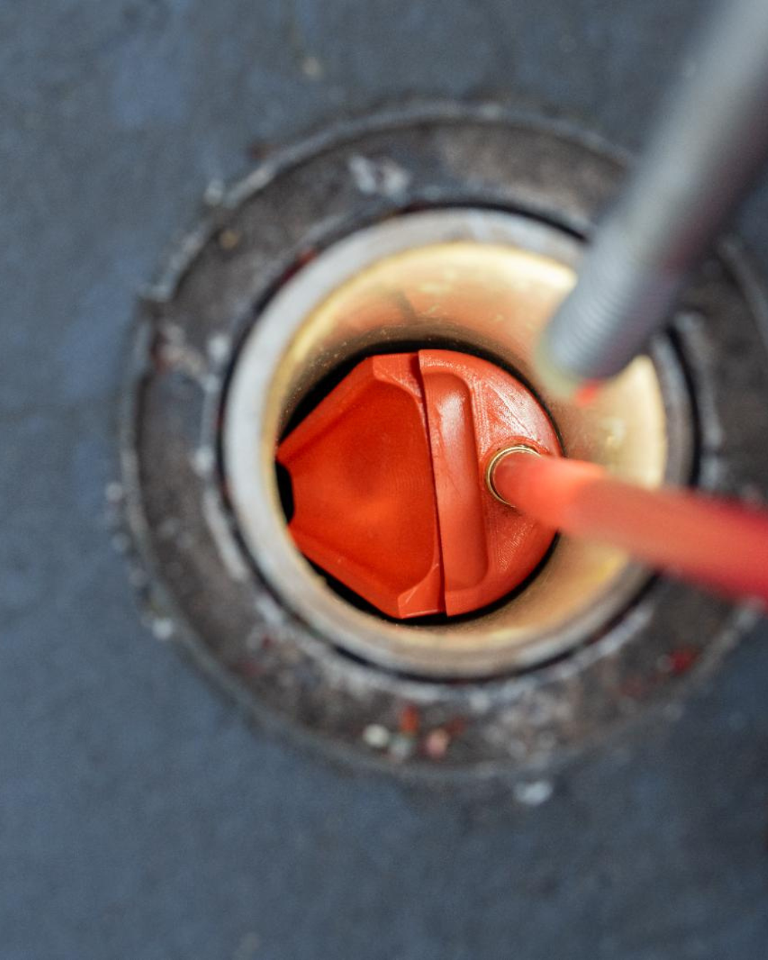 Close-up of an red pipe tool inserted into a metal drain opening