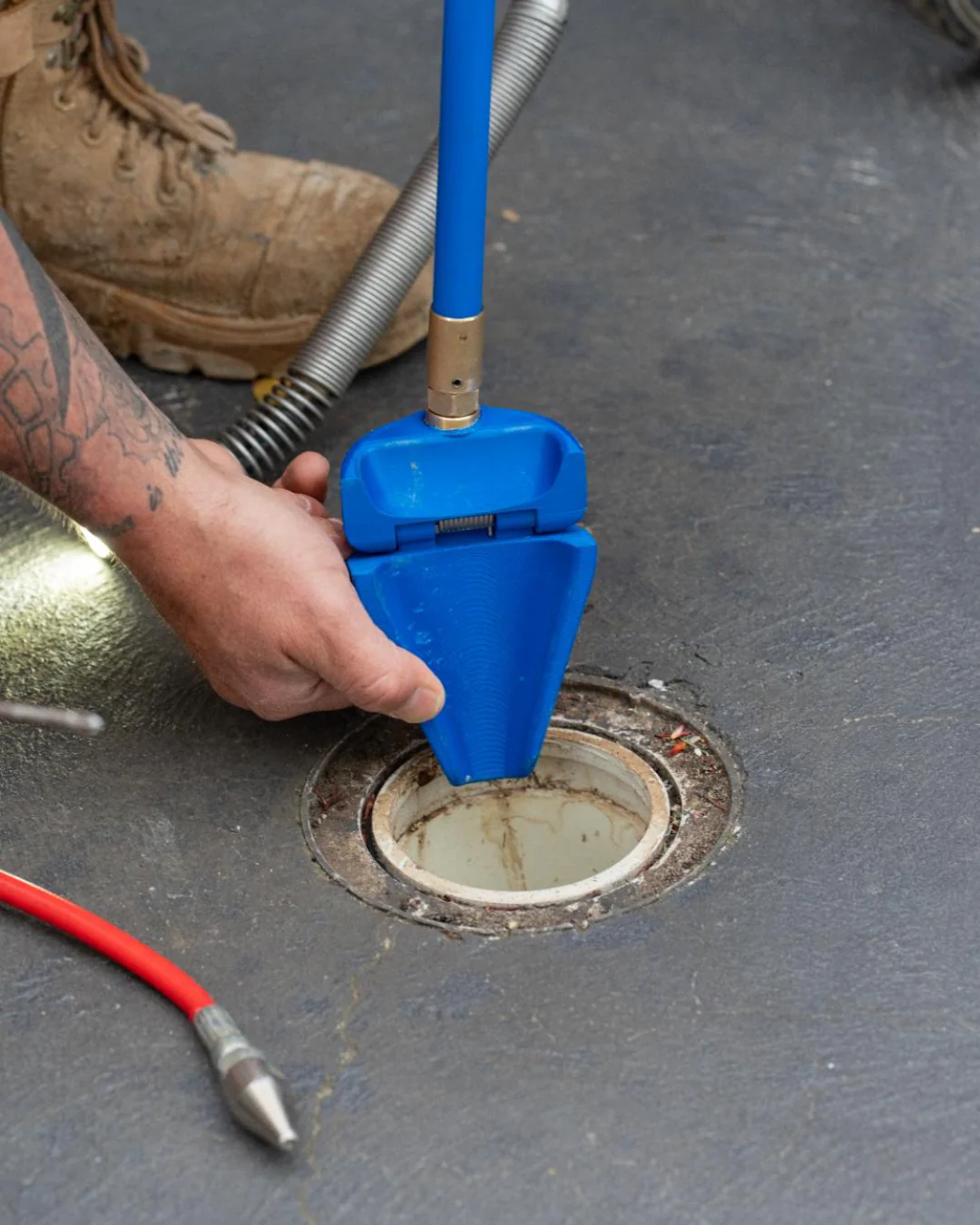 Person using a blue jet mate tool on a drain on a concrete floor.