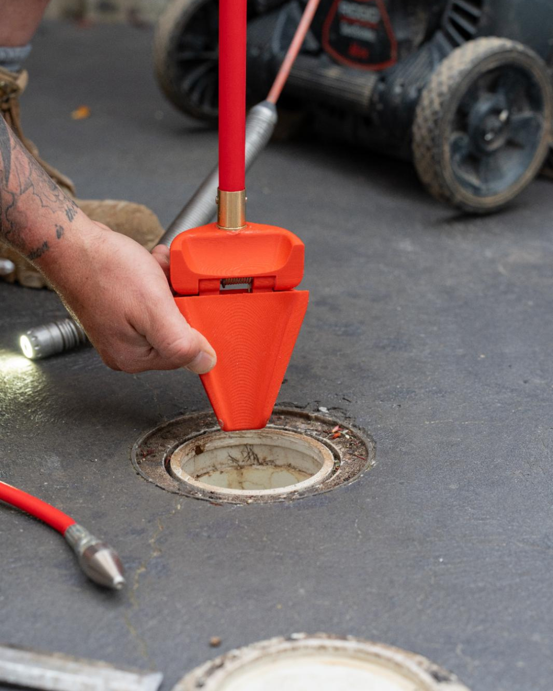 Person using a red tool to inspect a drain cover on a concrete surface.